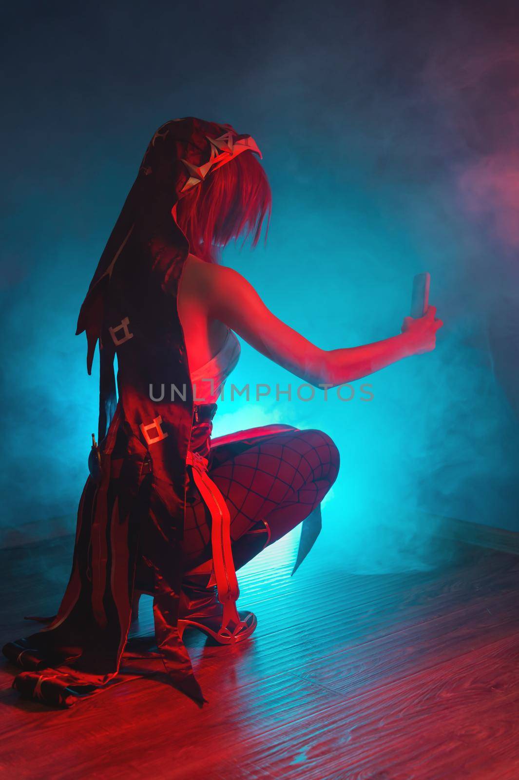 Vertical photo of a young girl in a cosplay costume sitting in a room with colored smoke and light and taking a selfie taking a video for social networks by yanik88
