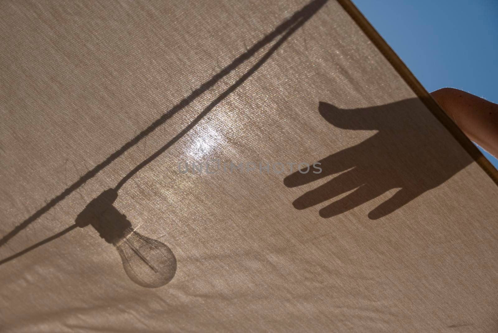 Hand touches light Bulb on tent creating shadow against the sun. Energy and ecological transition concept.