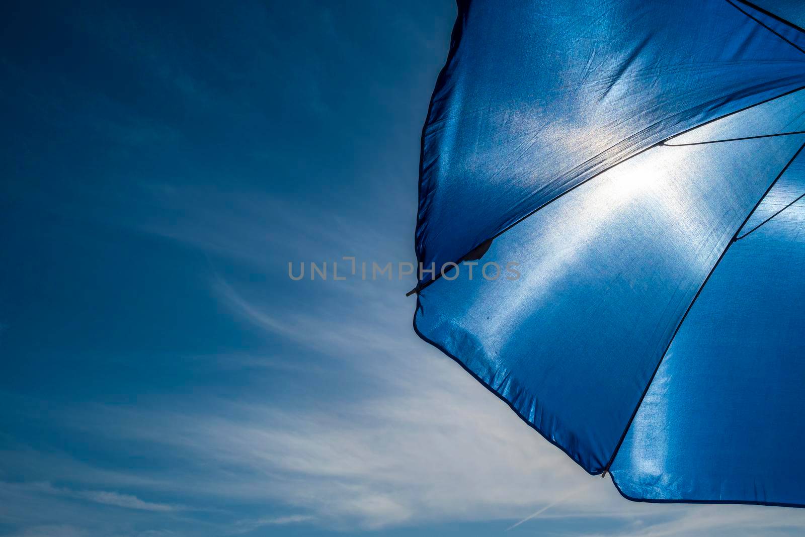 Vibrant blue beach umbrella against sun by SimmiSimons