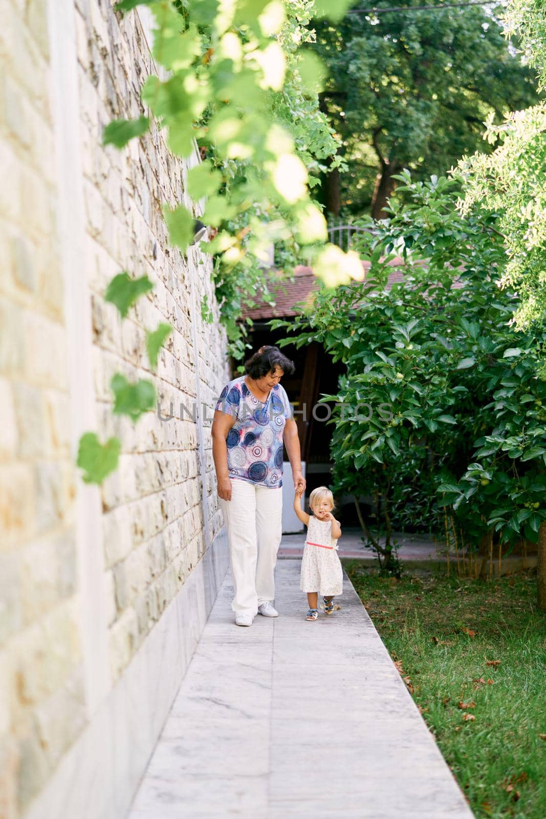 Grandmother with her little granddaughter walk holding hands against a stone wall in the garden. High quality photo
