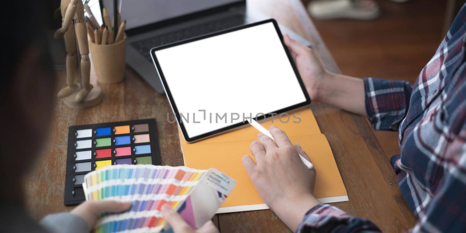 Teamwork of creative designers working on new project and choose color swatch samples for selection coloring on digital graphic tablet with work tools and equipment at workplace. by wichayada