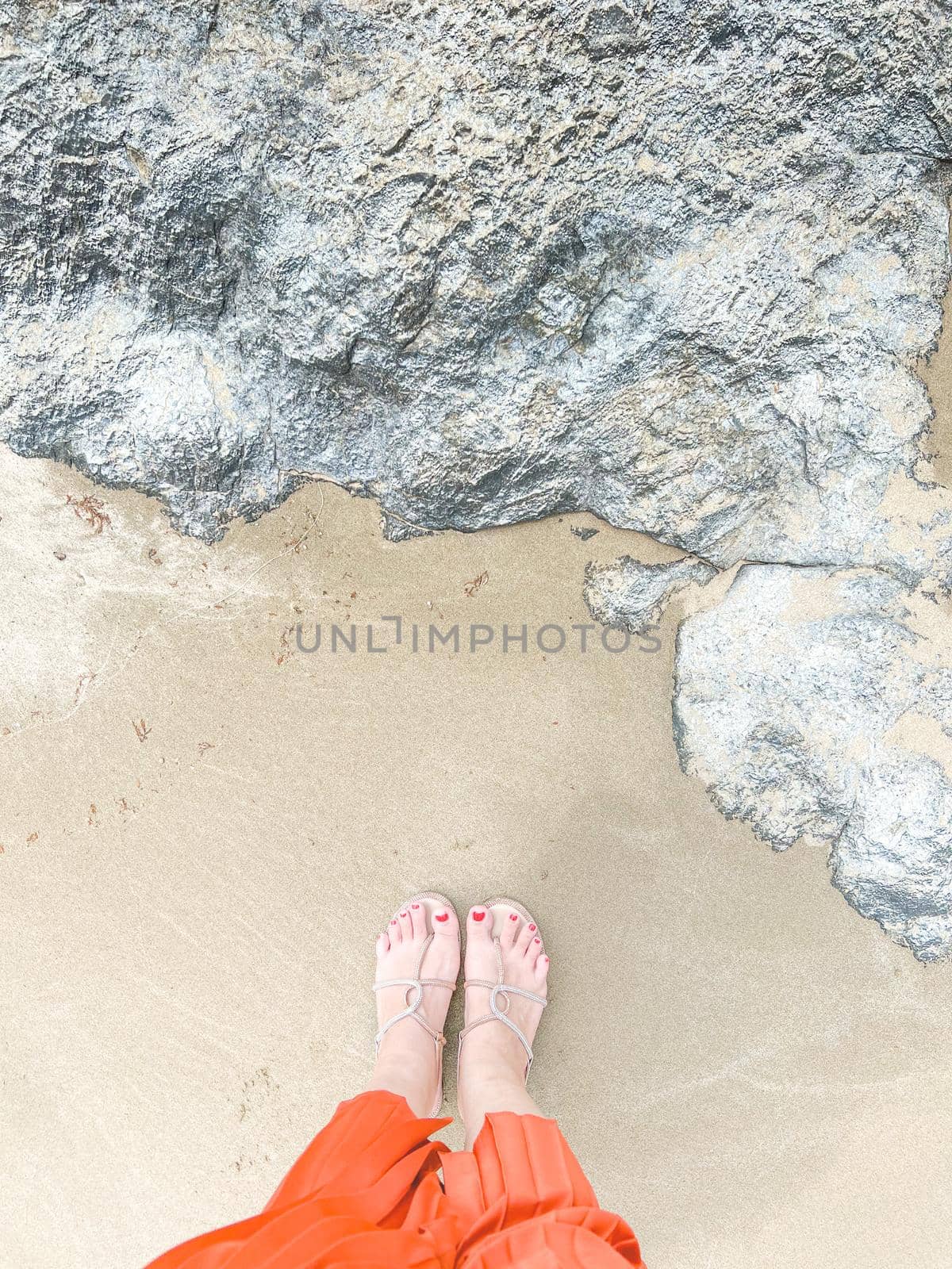 footed woman's legs standing on yellow sand on the beach with the big stone by makidotvn