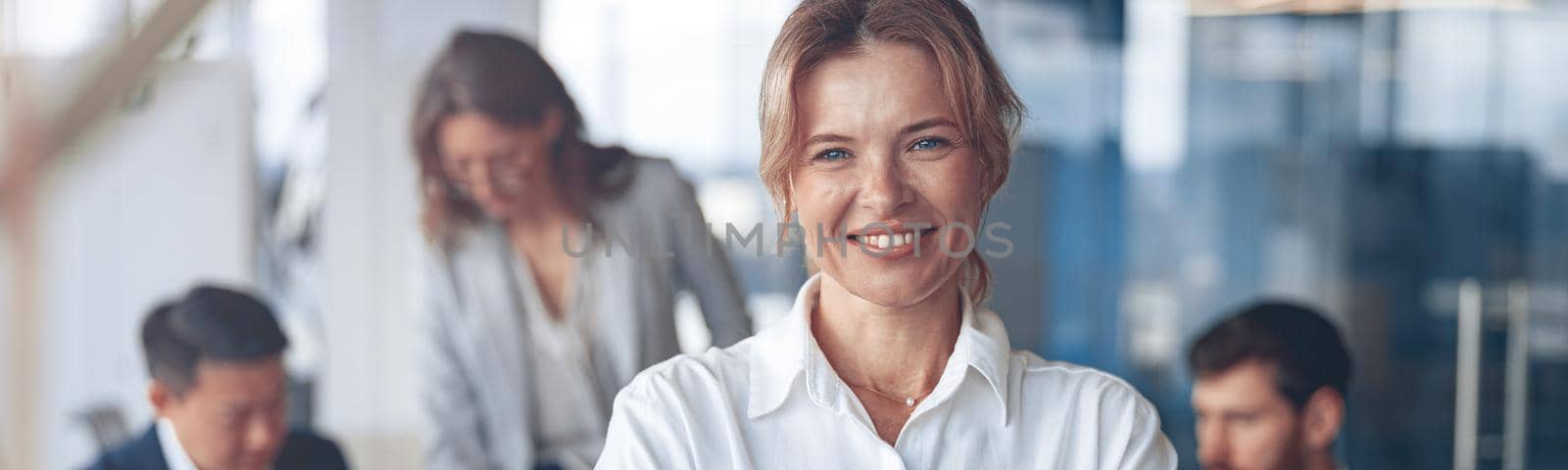 Portrait of beautiful smiling mature businesswoman with her colleagues on background in office by Yaroslav_astakhov