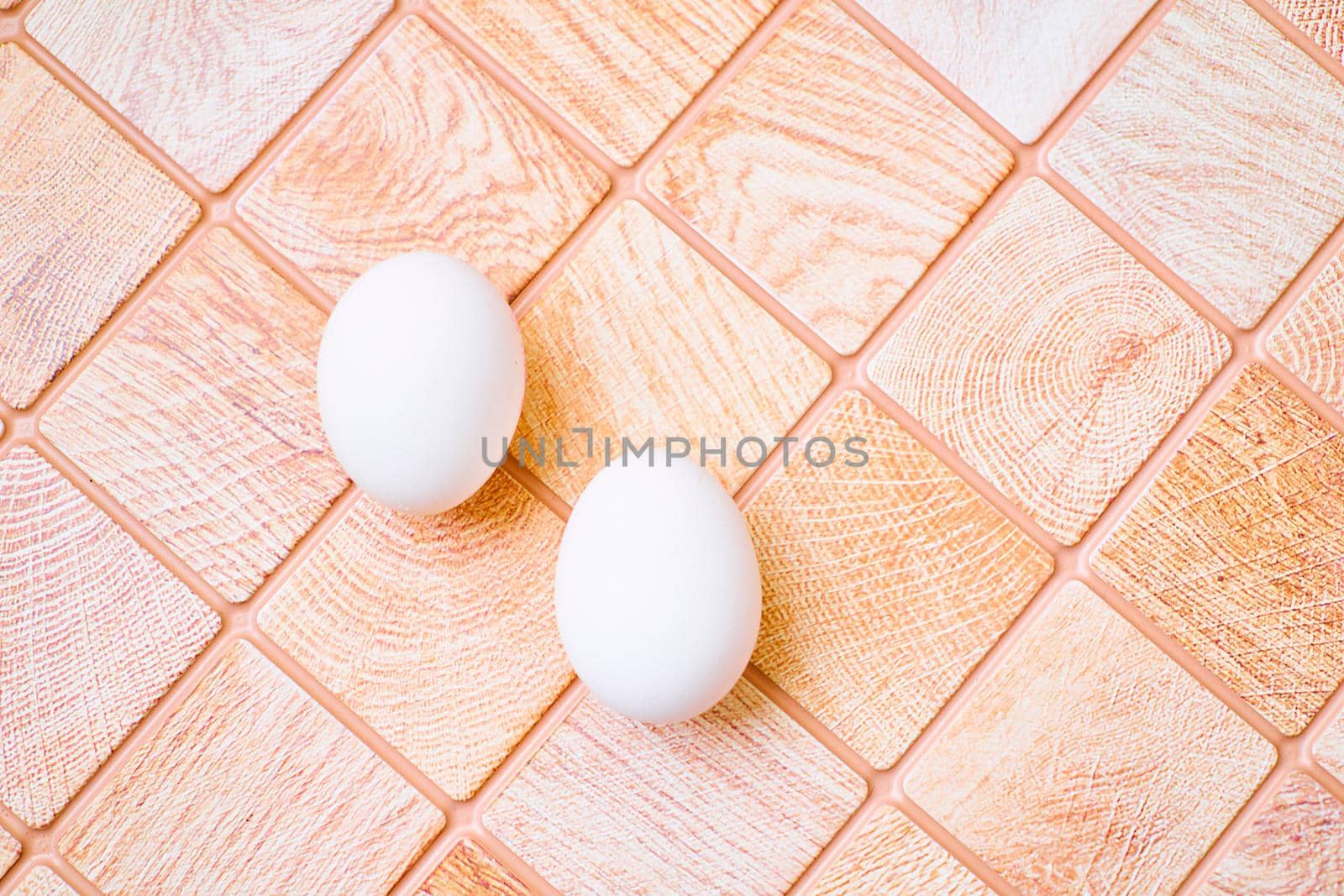 an oval or round object laid by a female bird, reptile, fish, or invertebrate, usually containing a developing embryo. Three chicken bird eggs on a wooden pink orange checkered surface.