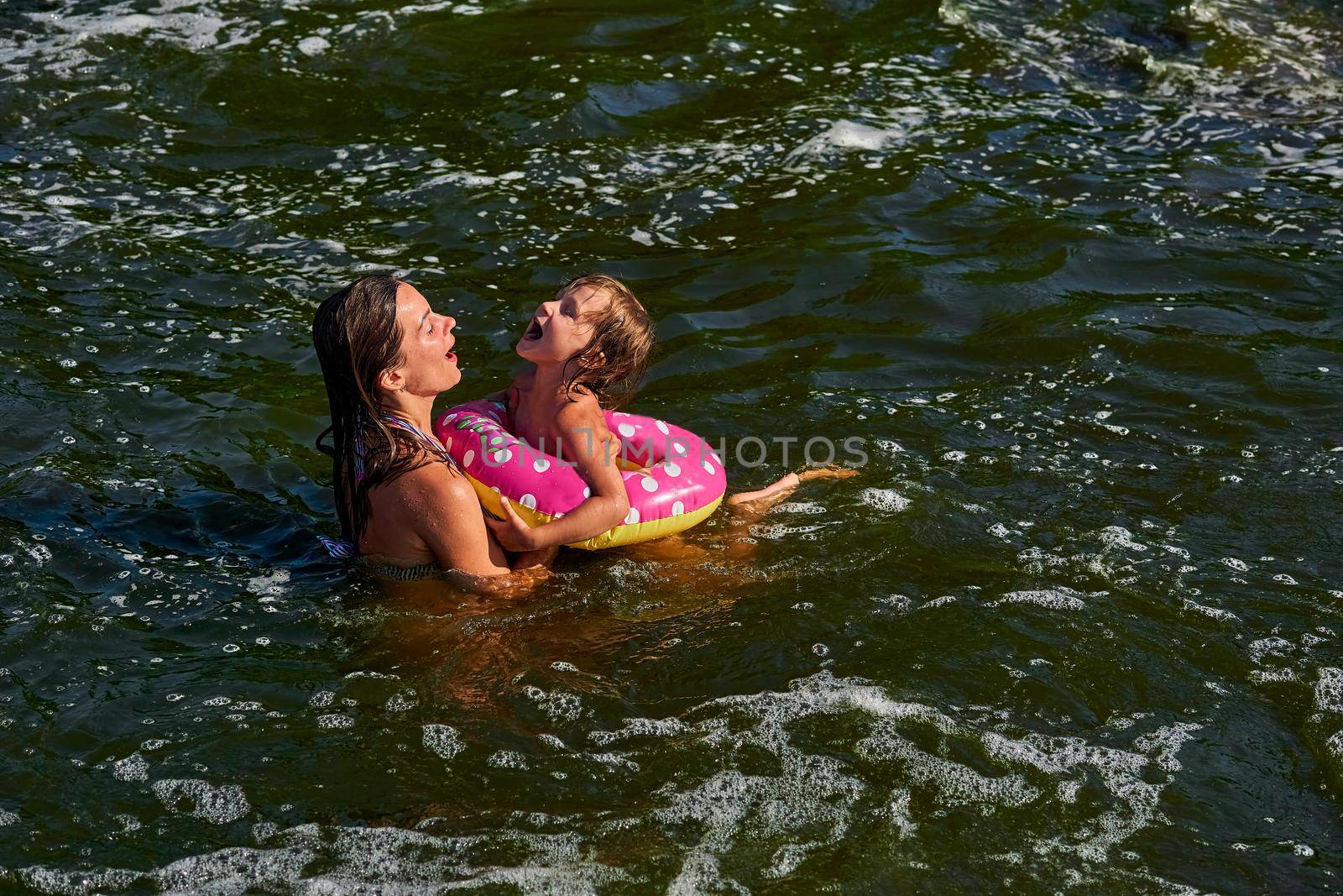 propel the body through water by using the limbs,by using fins, tail, or other bodily movement.Cute girl on a swimming circle bathes with her mother protecting her in the sea.