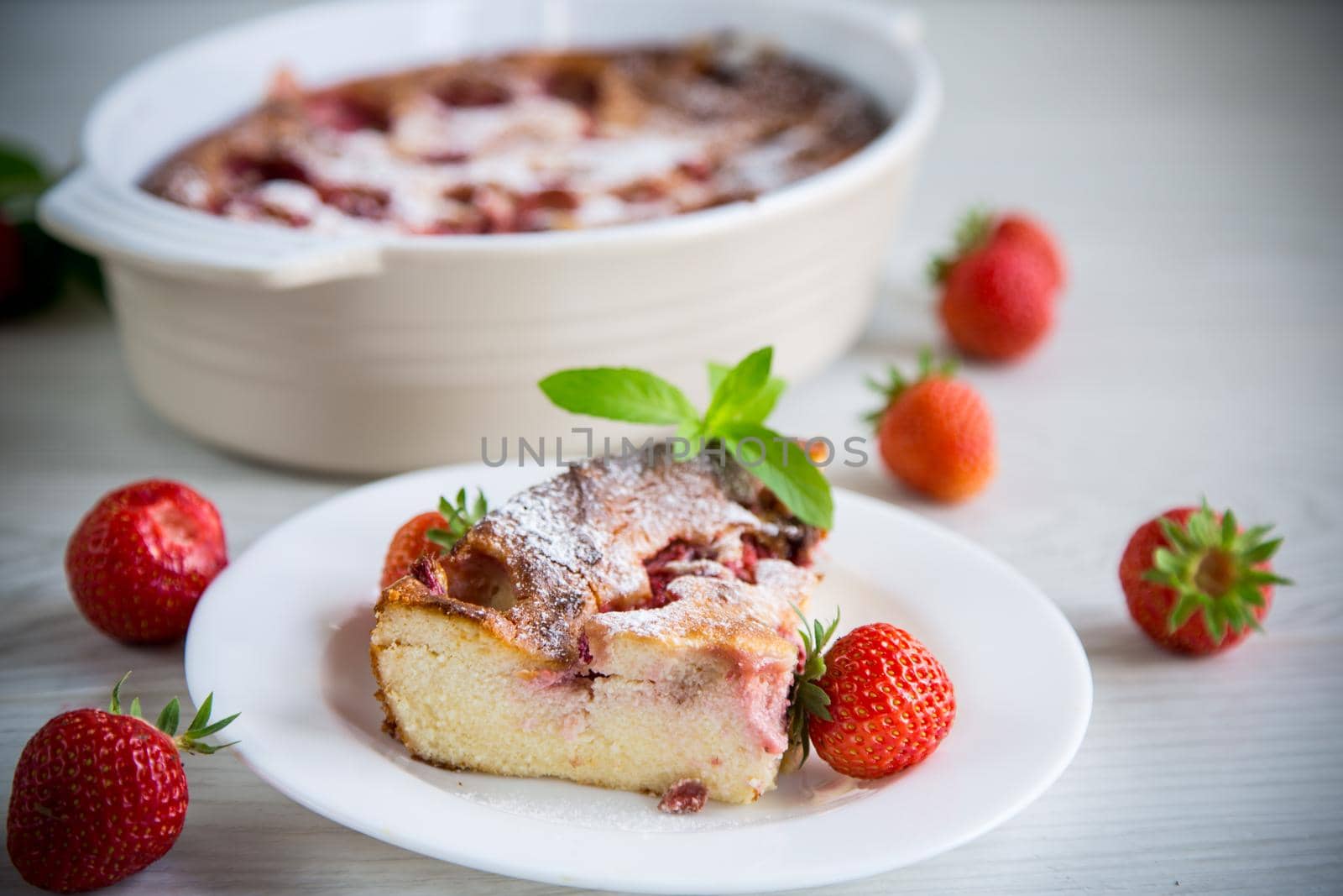Sweet cottage cheese casserole with strawberry filling, in a plate on a wooden table.