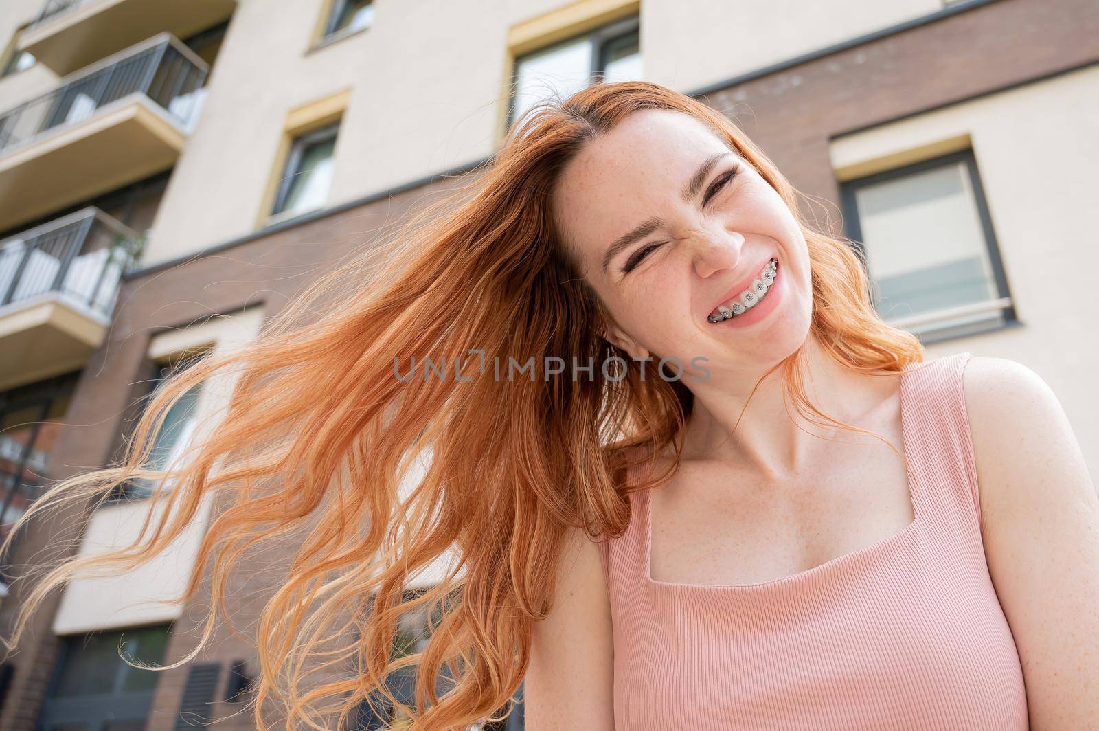 Beautiful young red-haired woman with braces on her teeth smiling in the summer outdoors.