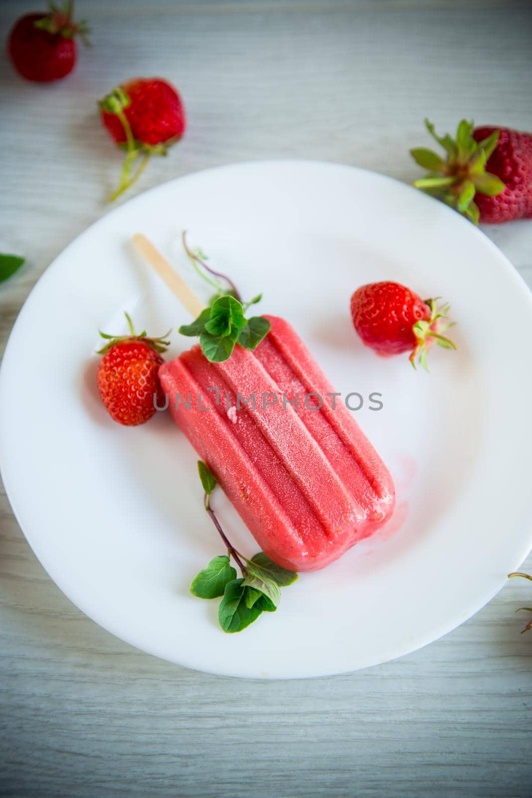 cooked homemade strawberry ice cream on a stick in a plate with strawberries