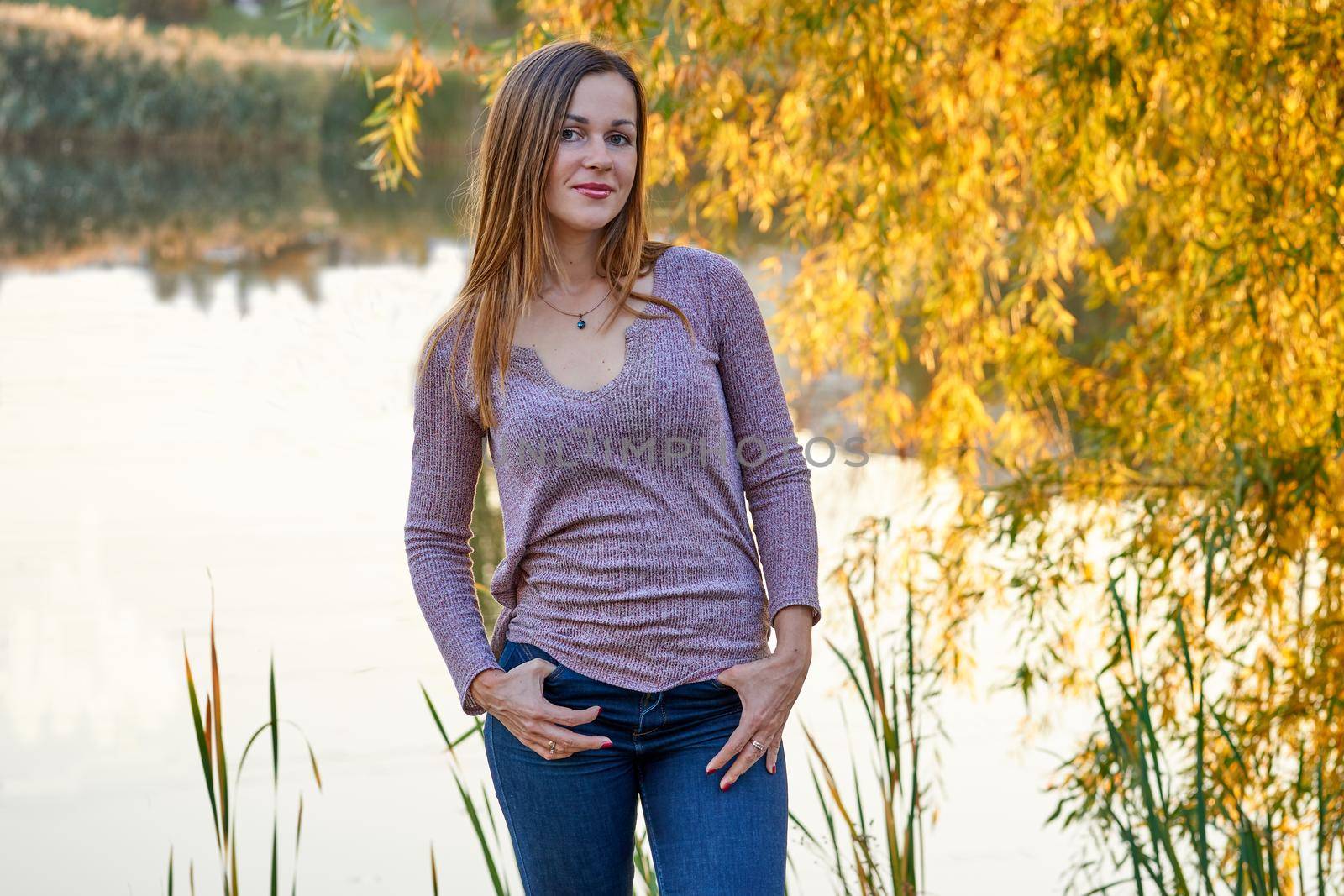 Young cheerful woman on the shore of a calm lake among golden autumn foliage by jovani68