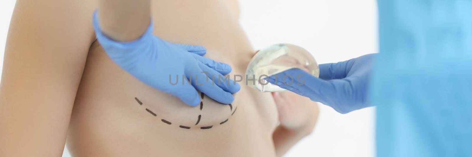 Close-up of doctor hold silicone breast implant and palping client breast. Woman topless in cabinet. Surgery, beauty, medicine, plastic operation concept