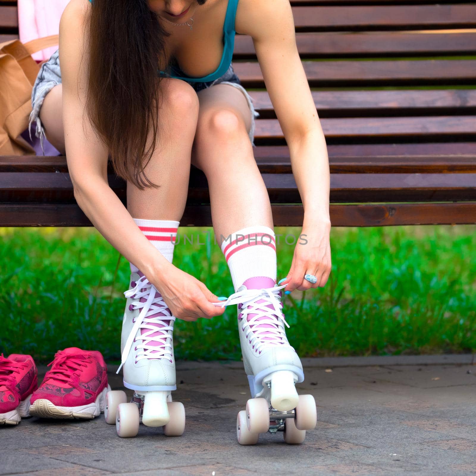 Female skater binds the roller skates on the bench in a park
