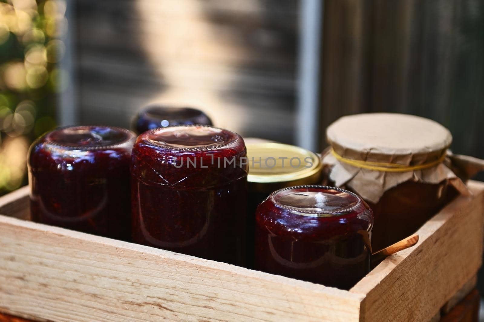Close-up of wooden crate with homemade berry jam, jelly, confiture and marmalade confiture in glass jars standing upside down against a wooden rustic background. Canning concept