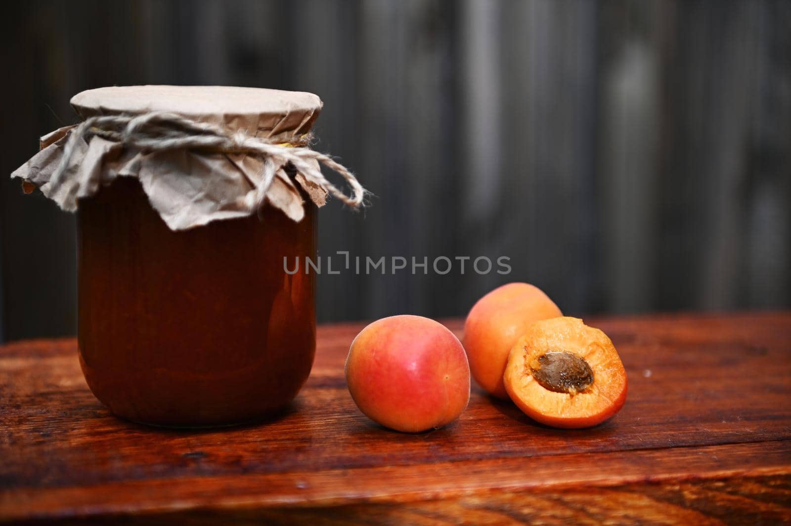 Still life. Close-up of a jar of homemade apricot confiture and ripe ready-to-eat apricots on a rustic wooden surface. Canning concept. Copy ad space for text