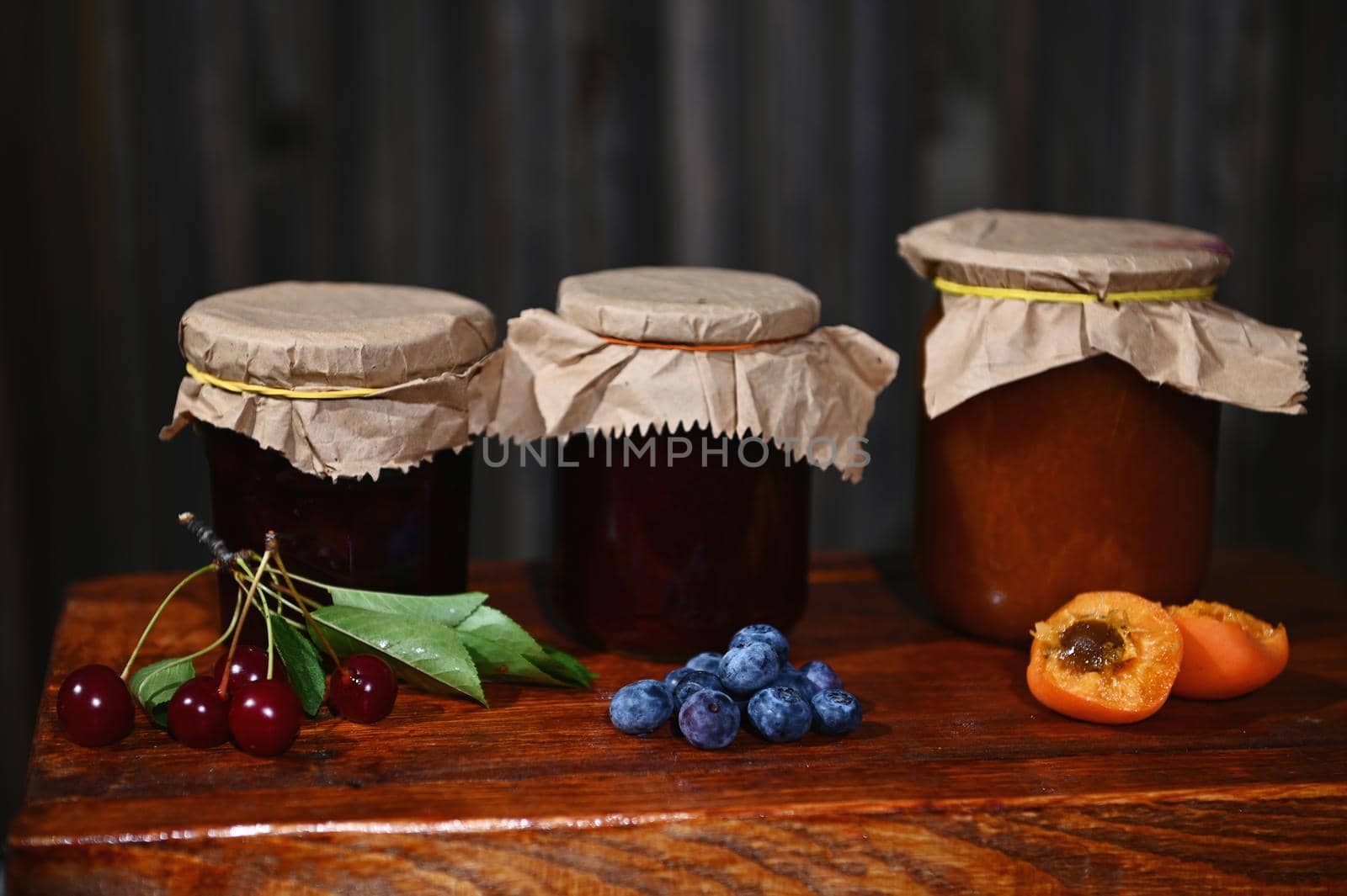 Assortment of homemade confitures of seasonal fruits and berries on rustic wooden background. Canning, preparation of preserved food for winter season. Still life, copy ad space