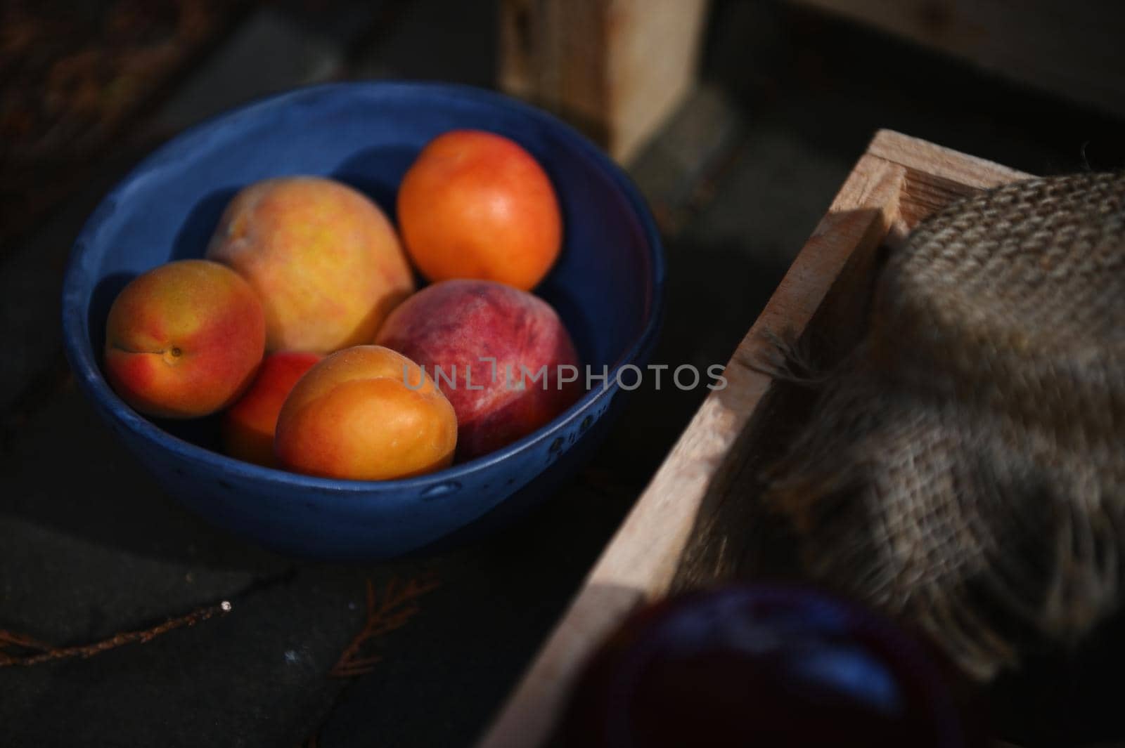 Focus on ripe, juicy, red, sunny and ready-to-eat apricots from organic farm in blue ceramic bowl next to a wooden box with homemade fruit jam jars. Healthy food, sweet canned food and canning concept