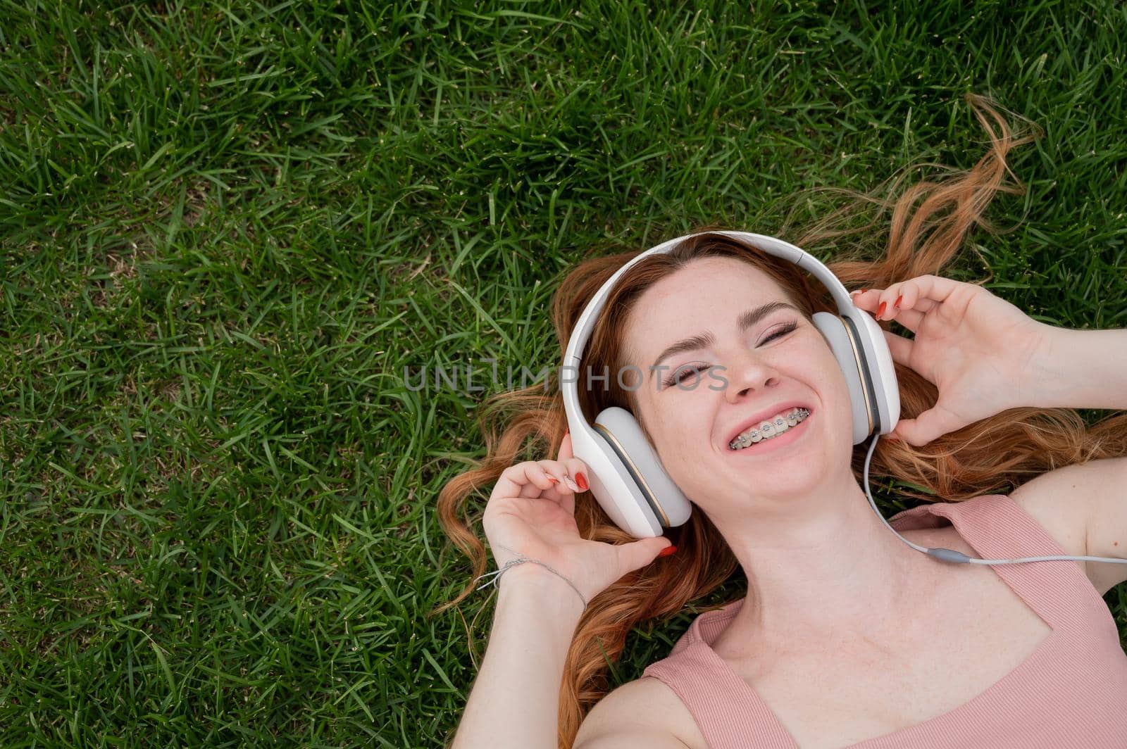 A young red-haired woman lies on the grass and listens to music