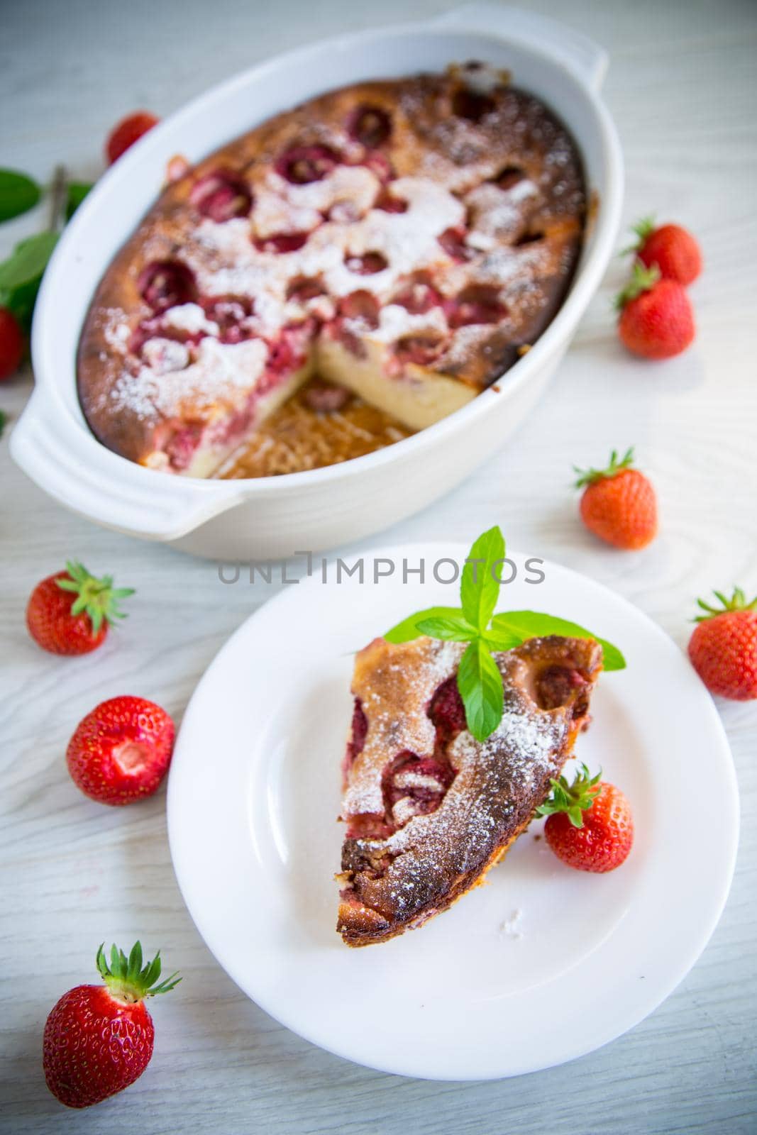 Sweet cottage cheese casserole with strawberry filling, in a plate on a wooden table.