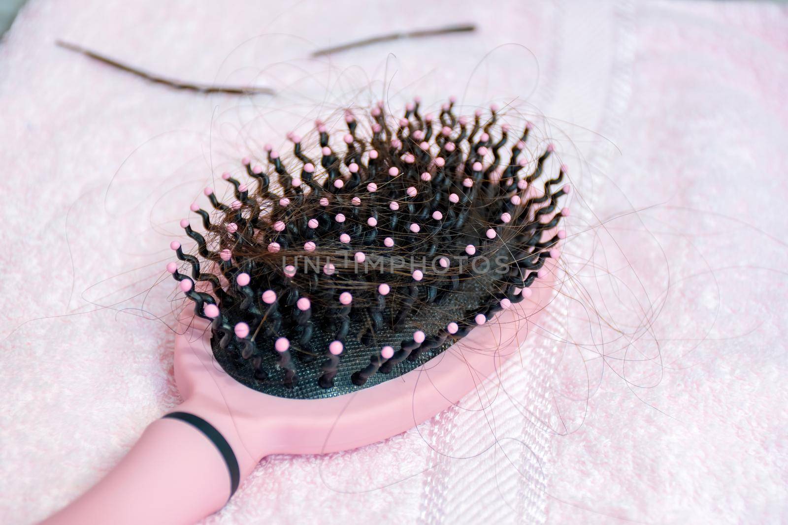 Hair loss concept. Hairbrush with brown fallen hairs on a pink towel.