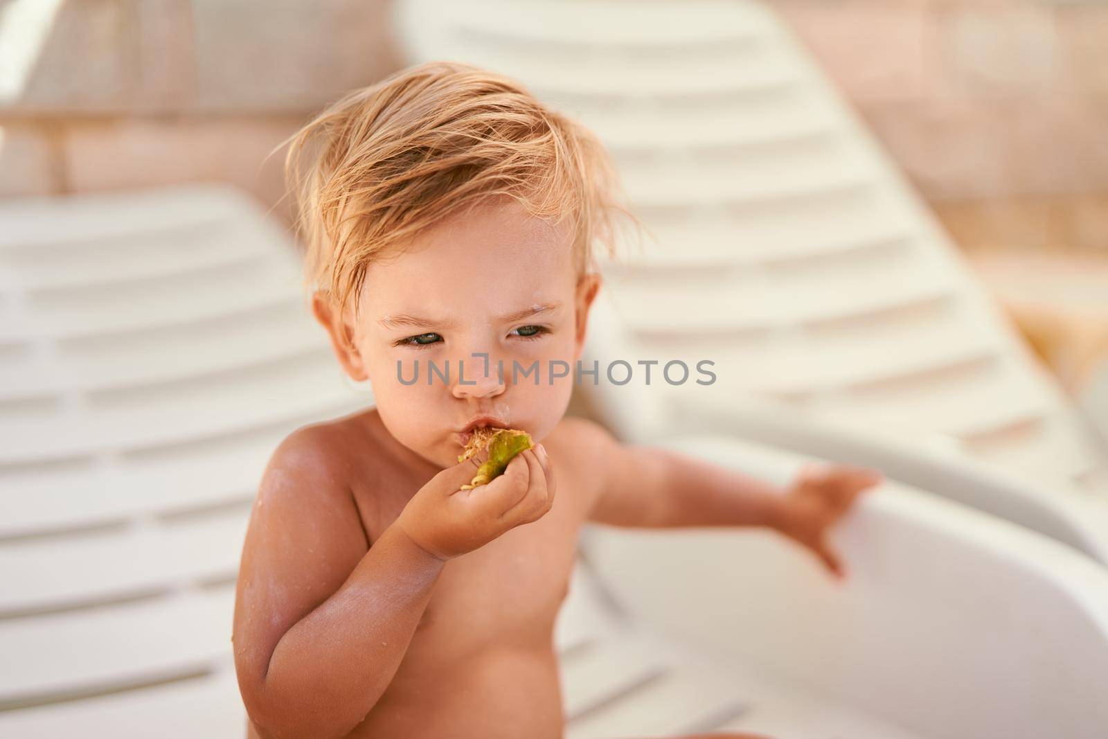 Little girl eating fruit while sitting on a sun lounger by Nadtochiy