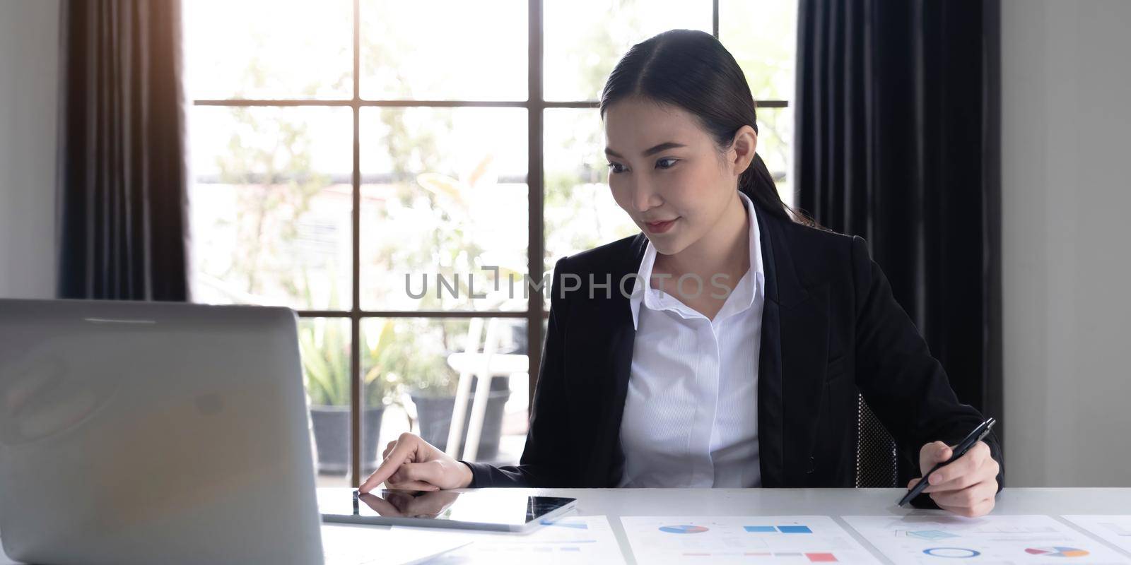 Portrait of Young Asian woman hand freelancer is working her job on computer tablet in modern office. Doing accounting analysis report real estate investment data, Financial and tax systems concept..