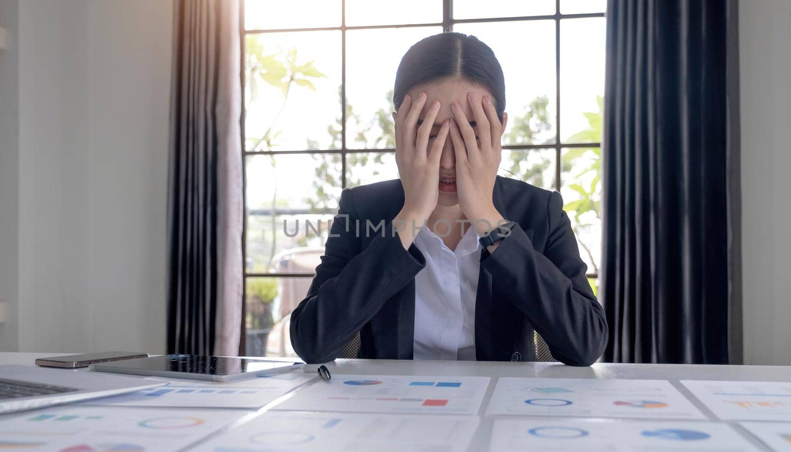 Young Asian businesswoman working on a tablet, is stressed has a headache and thinks hard at the office. by wichayada