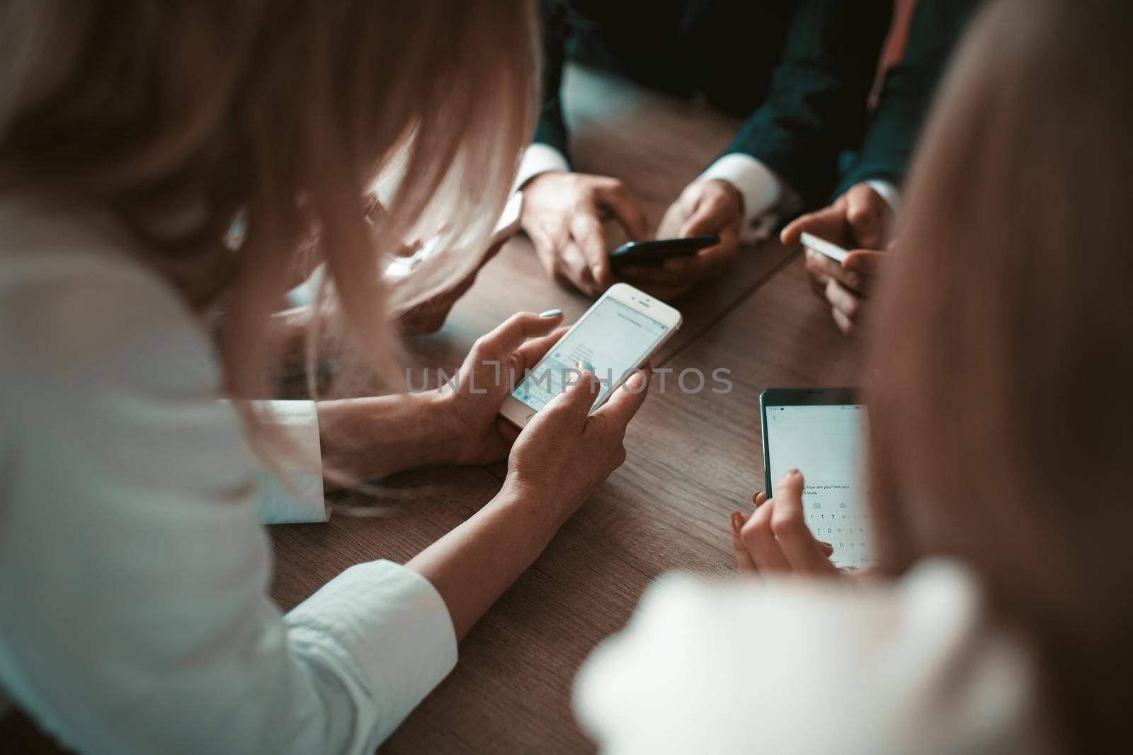 Business people chatting on mobile phones using text applications during business meeting. Rear view. June, 2018. Kyiv, Ukraine.