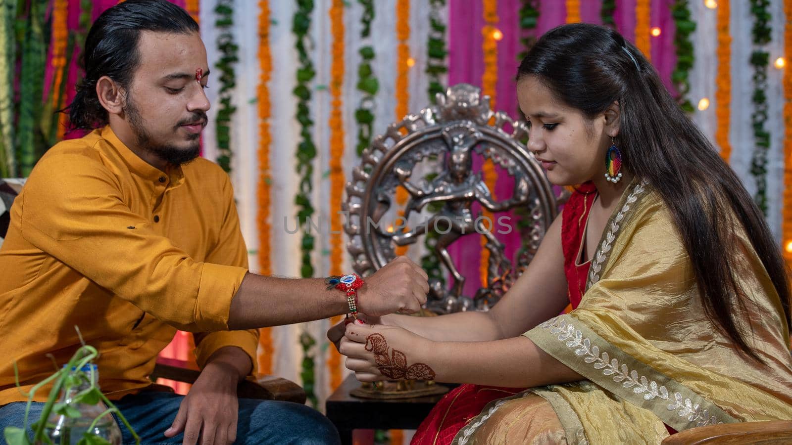 Sister tying the rakhi, Raksha Bandhan to brother's wrist during festival or ceremony - Raksha Bandhan celebrated across India as selfless love or relationship between brother and sister