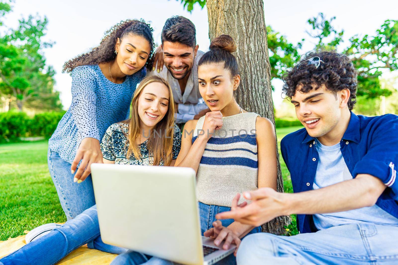 Young hipster friends group sitting on grass in city park making surprise faces looking laptop screen. Modern fun concept with millenials on new trends and technology. Wireless and social media by robbyfontanesi