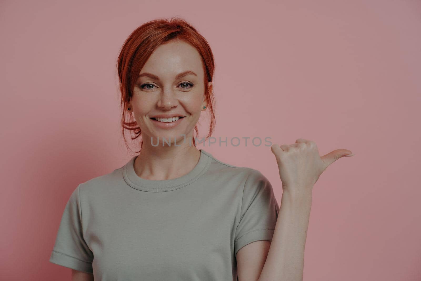 Cheerful redhead woman with happy facial expression indicating with finger at blank copy space by vkstock