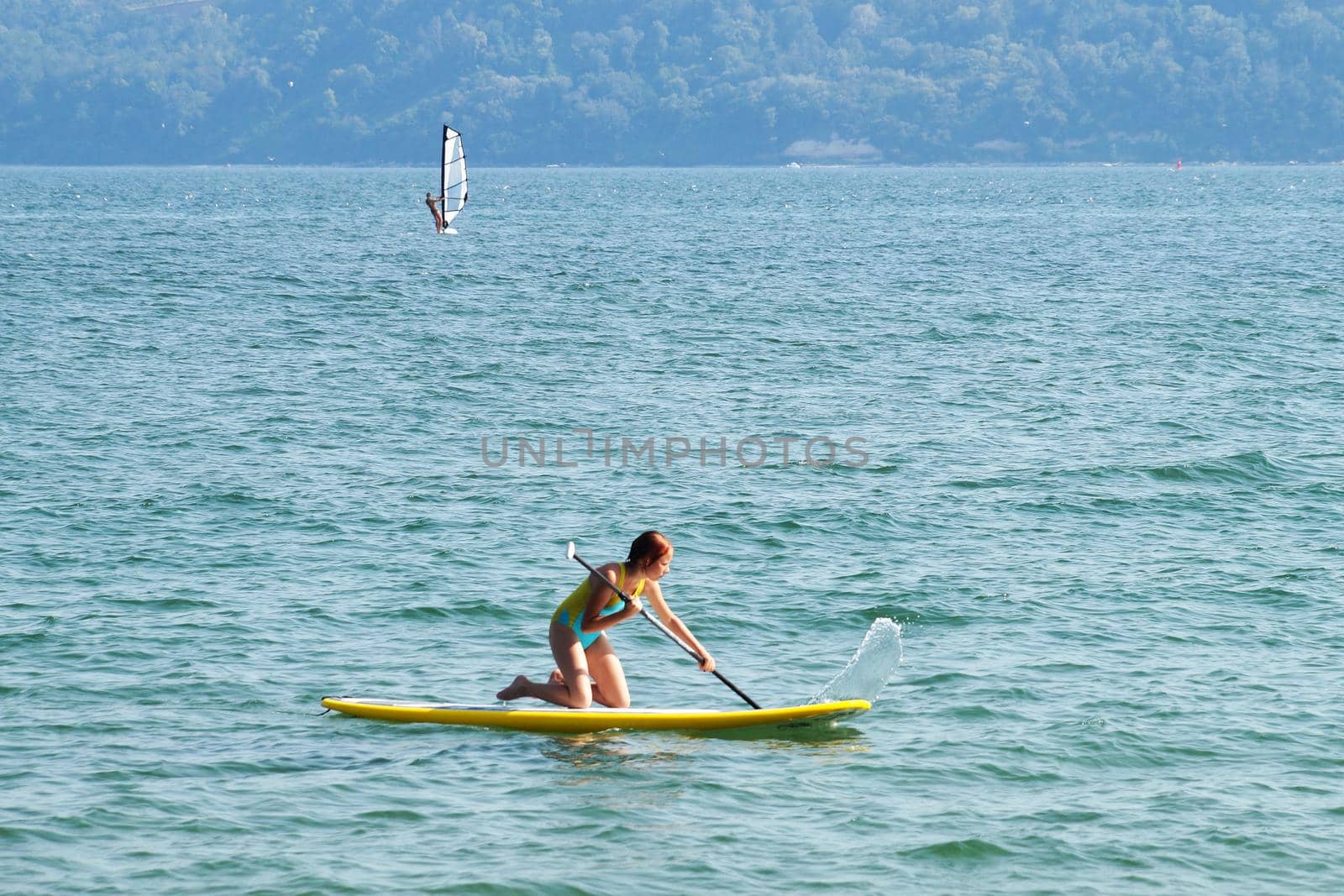 teenage girl riding a supboard in the sea on her knees.