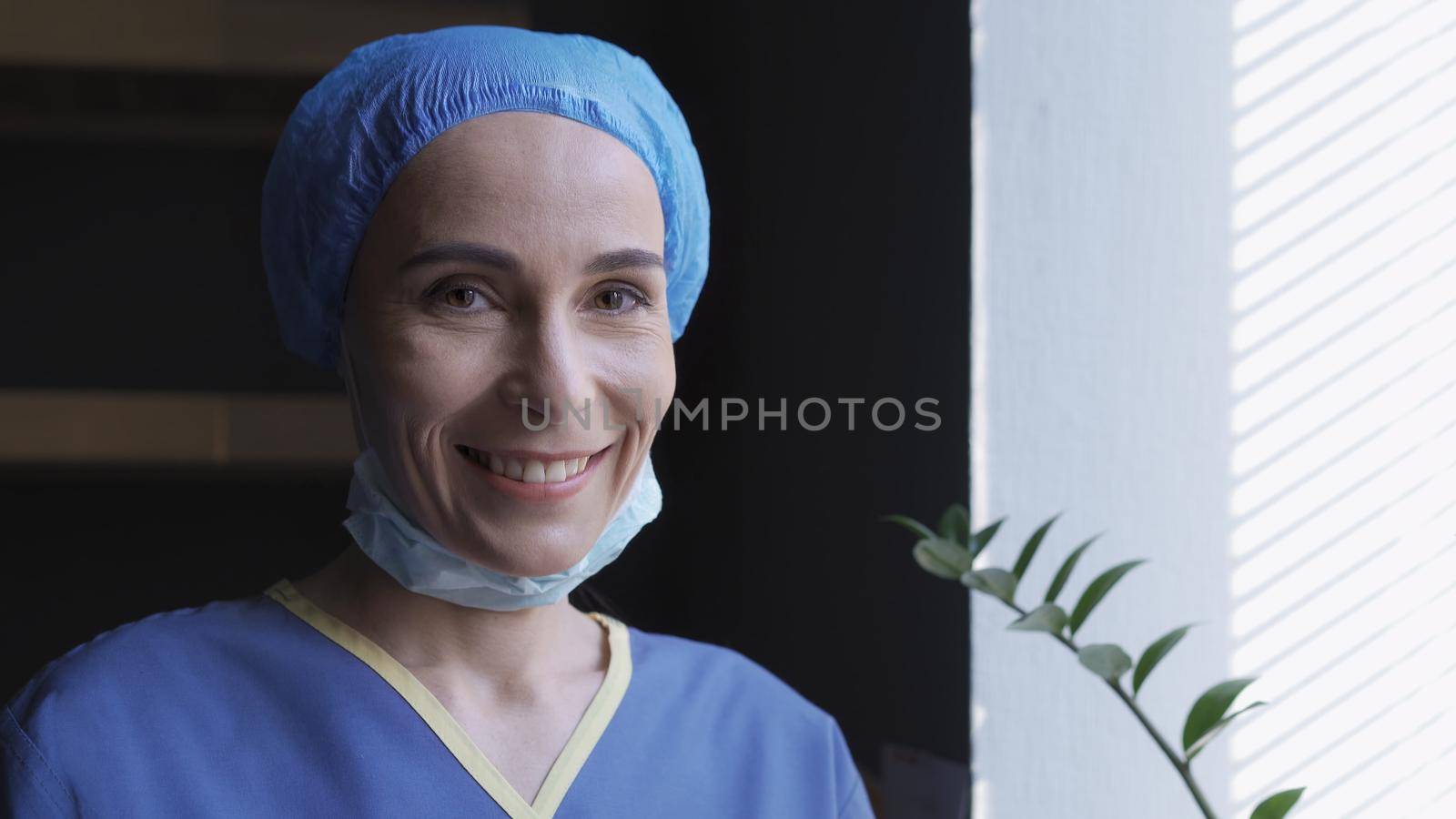 Smiling Female Doctor Rejoices Standing Near Window by LipikStockMedia