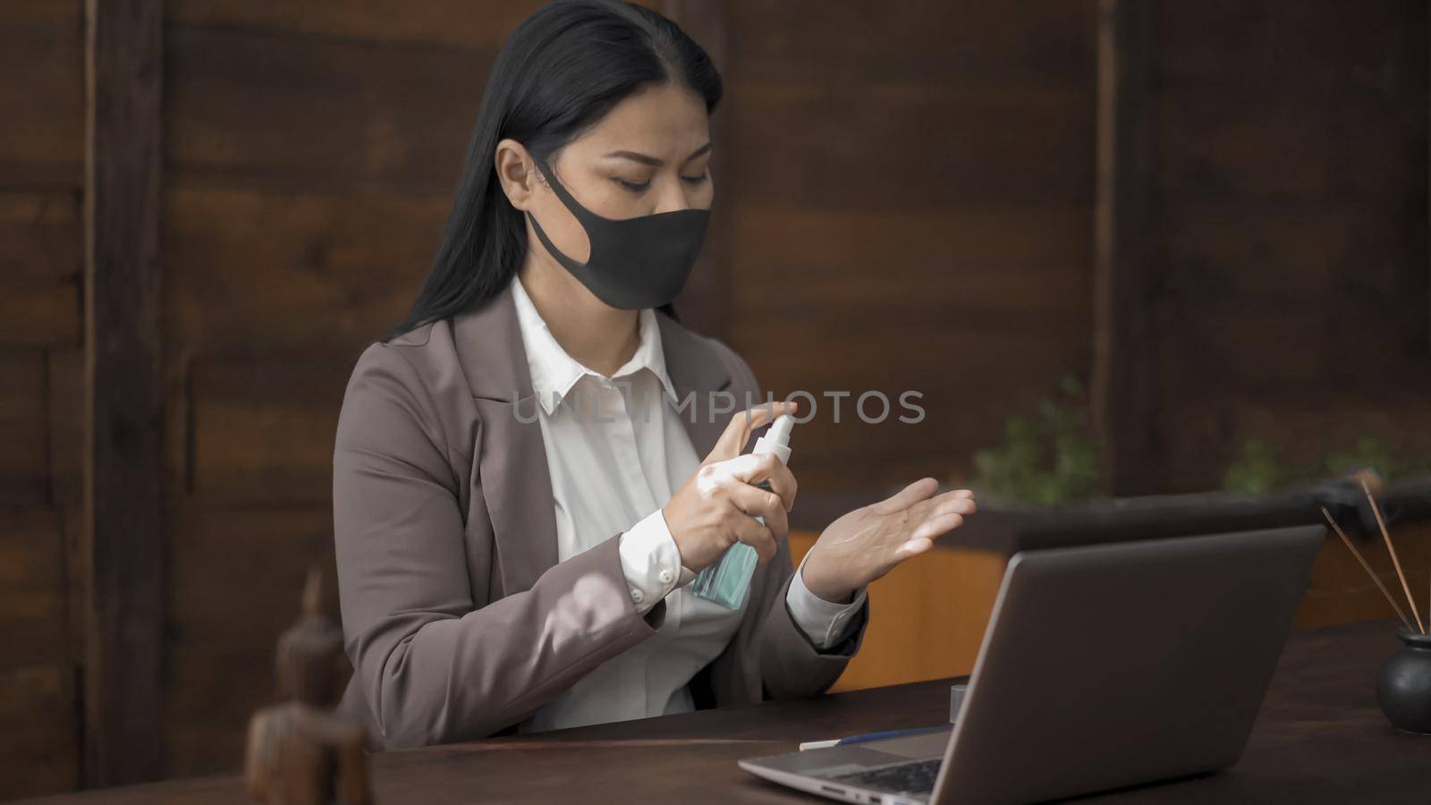 Business Woman In Mask Disinfects Hands Sitting At Office Desk, Asian Brunette Woman Sprinkles With Sanitizer Spray On Hands For Disinfection While Working With Computer In Office During Quarantine