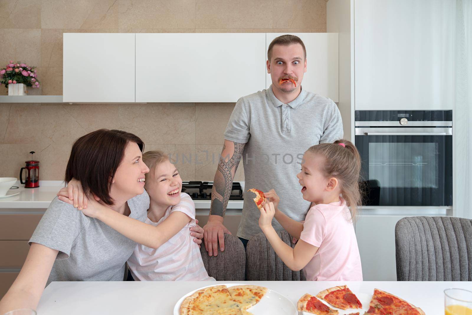 Smiling Family Dining Together at kitchen table and having fun, parents with two daughters by Mariakray