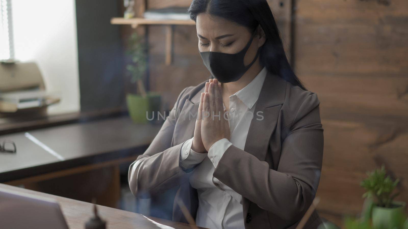 Businesswoman In Protective Mask Prays Alone In Office by LipikStockMedia