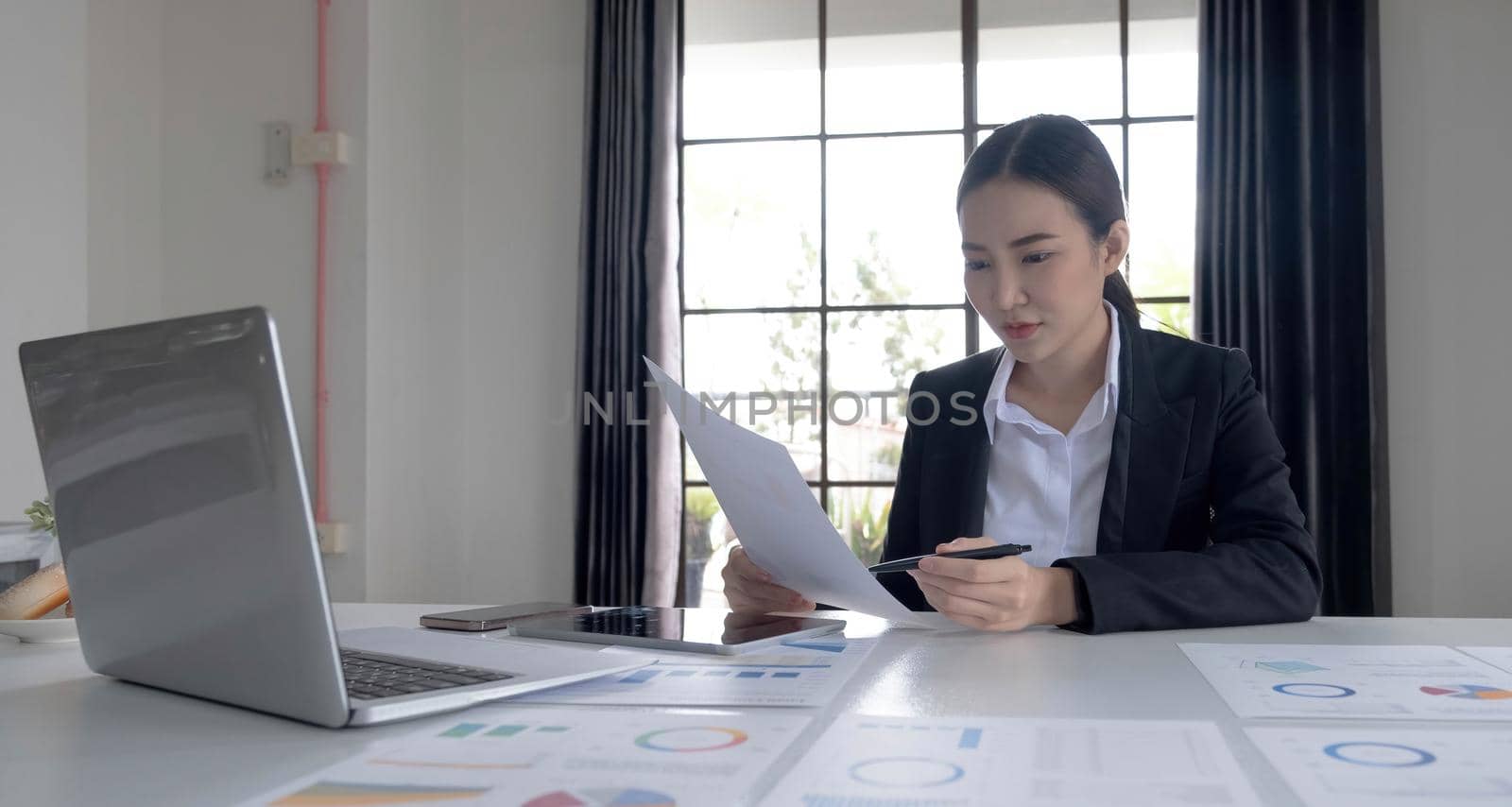 Portrait of an Asian woman working on a tablet computer in a modern office. Make an account analysis report. real estate investment information financial and tax system concepts.