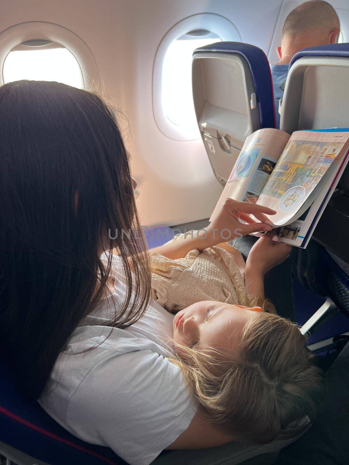 Mom with a sleeping daughter sits in an airplane seat and reads a magazine. High quality photo