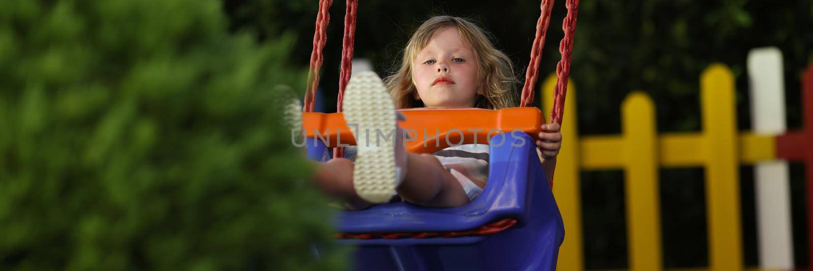 Portrait of little girl having fun on swing on playground in park alone. Pretty kid enjoy ride outdoors, place for children. Childhood, nature, joy concept