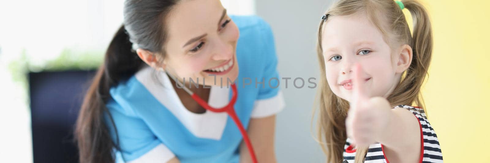 Portrait of girl being examined by pediatrician doctor, happy child show thumbs up gesture. Cheerful kid on checkup. Medicine, appointment, help concept