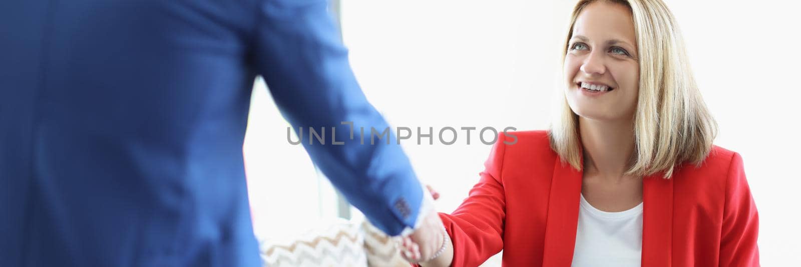Portrait of cheerful blonde young lady greeting man with handshake sitting on sofa. Business meeting to discuss agreement. Deal, lunch time, career concept