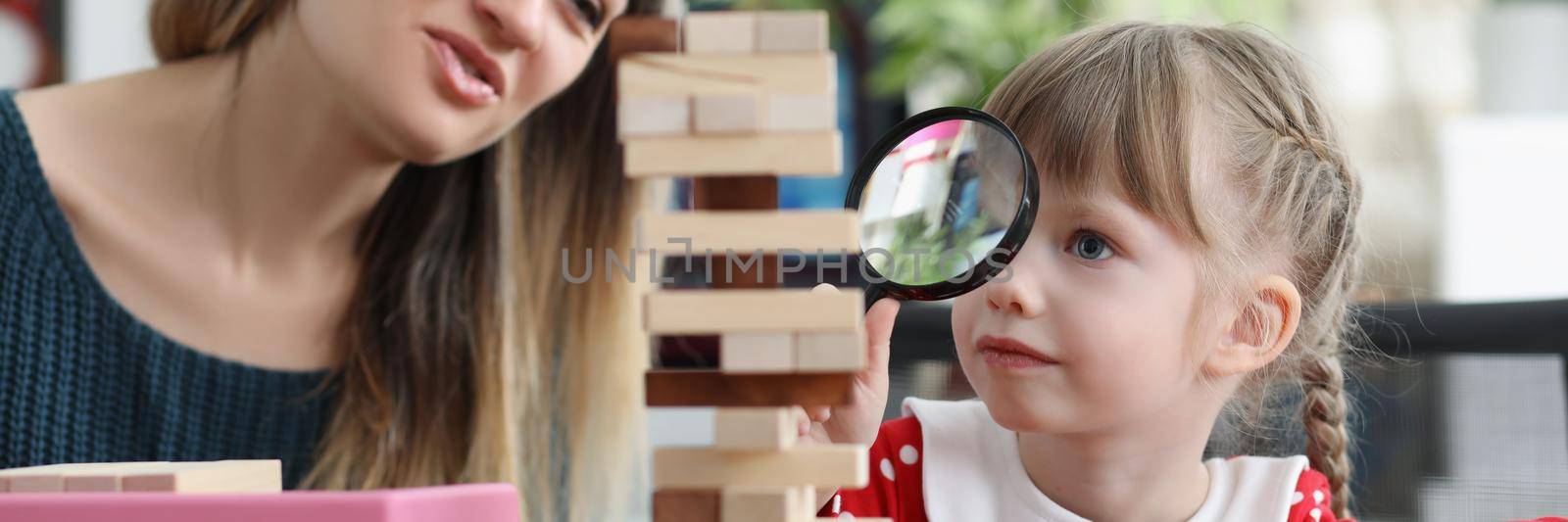 Portrait of cute little girl watch through magnifying glass on high wooden tower. Help child in development, improve concentration. Home education concept
