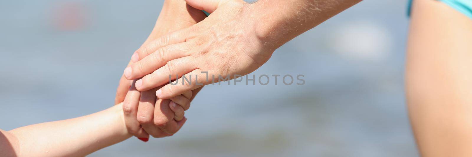 Close-up of family holding hands, mother father and child walking on coastline. Cropped picture of warm and lovable relationships in family. Love concept