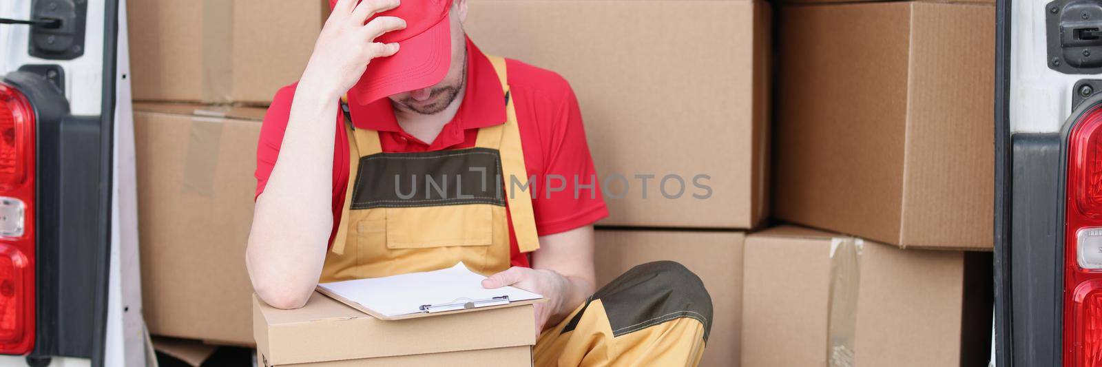 Close-up of delivery man sit in van with delivery receipt and wait for client. Middle aged courier in red uniform. Fast shipping, address delivery concept