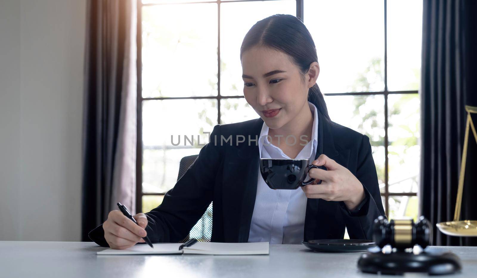 Professional Asian female lawyer working in her office, sipping a morning coffee while reading a law contract. cropped image by wichayada