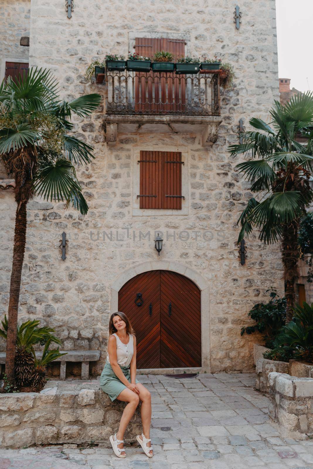 Girl Tourist Resting in the Ancient Narrow Street On A Beautiful Summer Day In MEDITERRANEAN MEDIEVAL CITY, OLD TOWN KOTOR, MONTENEGRO. Young Beautiful Cheerful Woman Walking On Old Street. Europe by Andrii_Ko