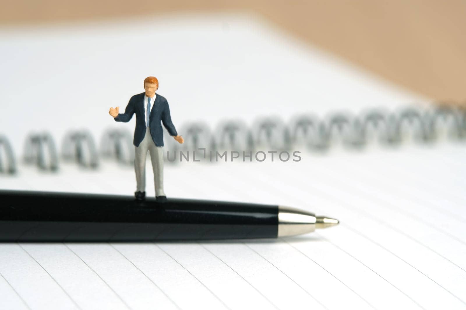 Miniature people toy figure photography. Signing agreement concept. A shrugging businessman stand above a black pen and opened document on wooden desk. Image photo