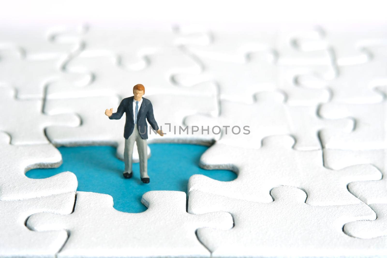 Miniature people toy figure photography. A shrugging businessman standing above missing piece of puzzle jigsaw. Image photo