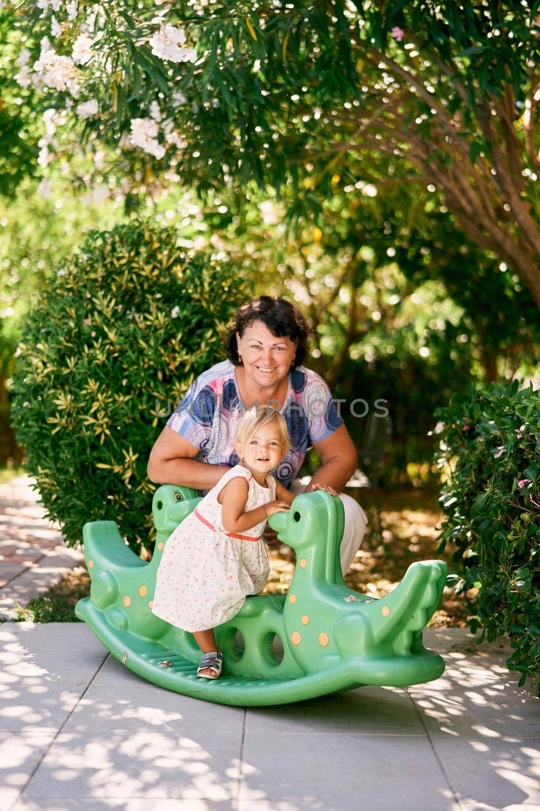 Grandmother squatted near a little girl on a teeter-totter in the green park. High quality photo