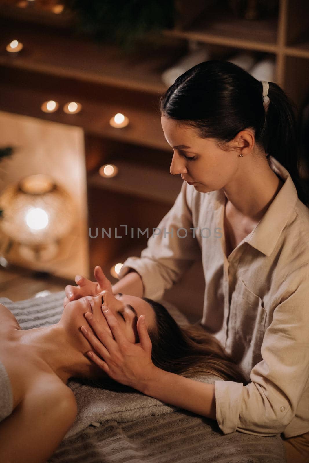 A cosmetologist girl does a facial and neck massage to a girl in the office for skin elasticity.