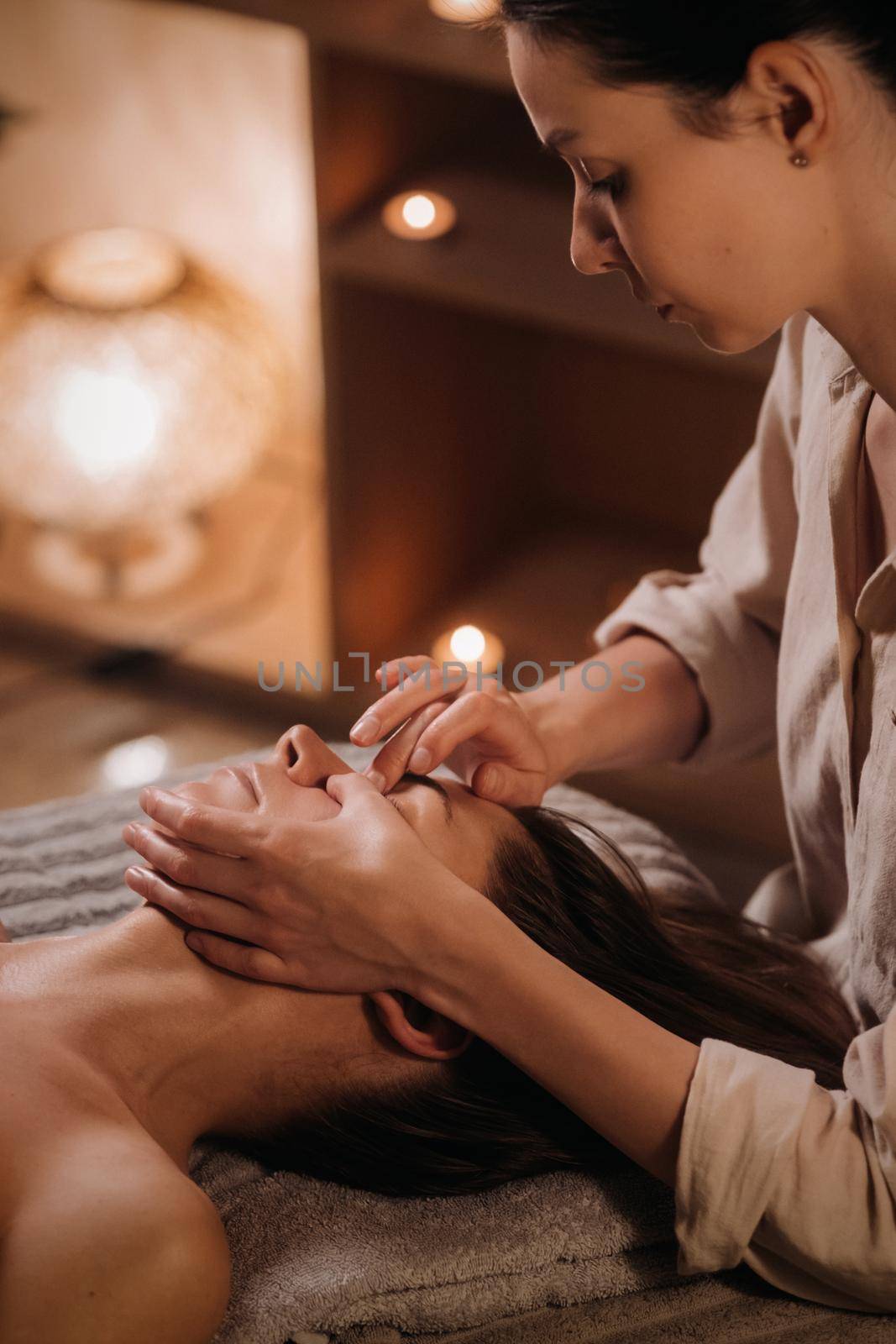 A cosmetologist girl does a facial and neck massage to a girl in the office for skin elasticity.