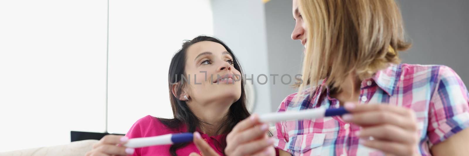 Portrait of best friends hold pregnancy tests, women celebrate big news. Smiling sisters look at each other. Pregnancy, new period, life change concept